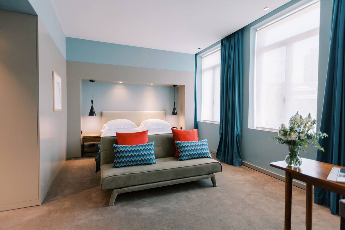 Une chambre d’hôtel moderne équipée d’un lit, d’un canapé, d’une table de chevet et d’une fenêtre avec des rideaux.