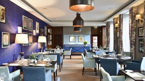 A hotel dining area with blue walls, framed artwork, and modern lighting fixtures.