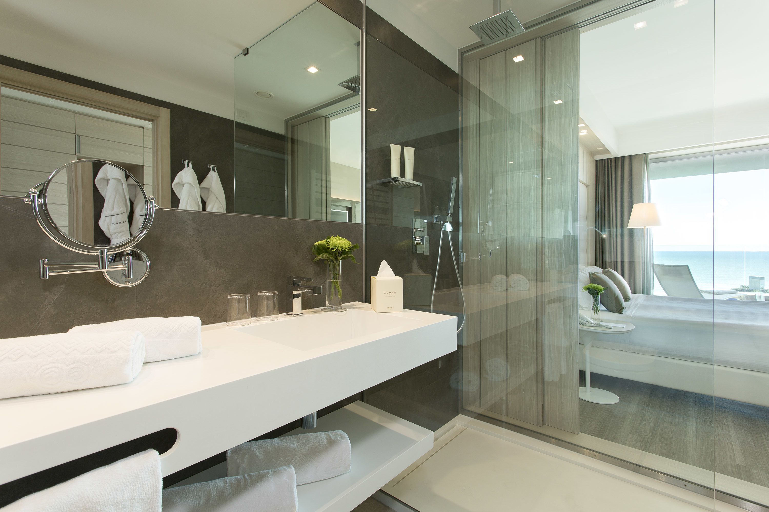 A modern bathroom with a large mirror, white countertop, and a glass-enclosed shower area.