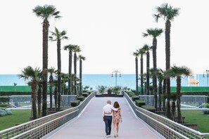 Una pareja caminando sobre un puente, con palmeras y vista al mar.