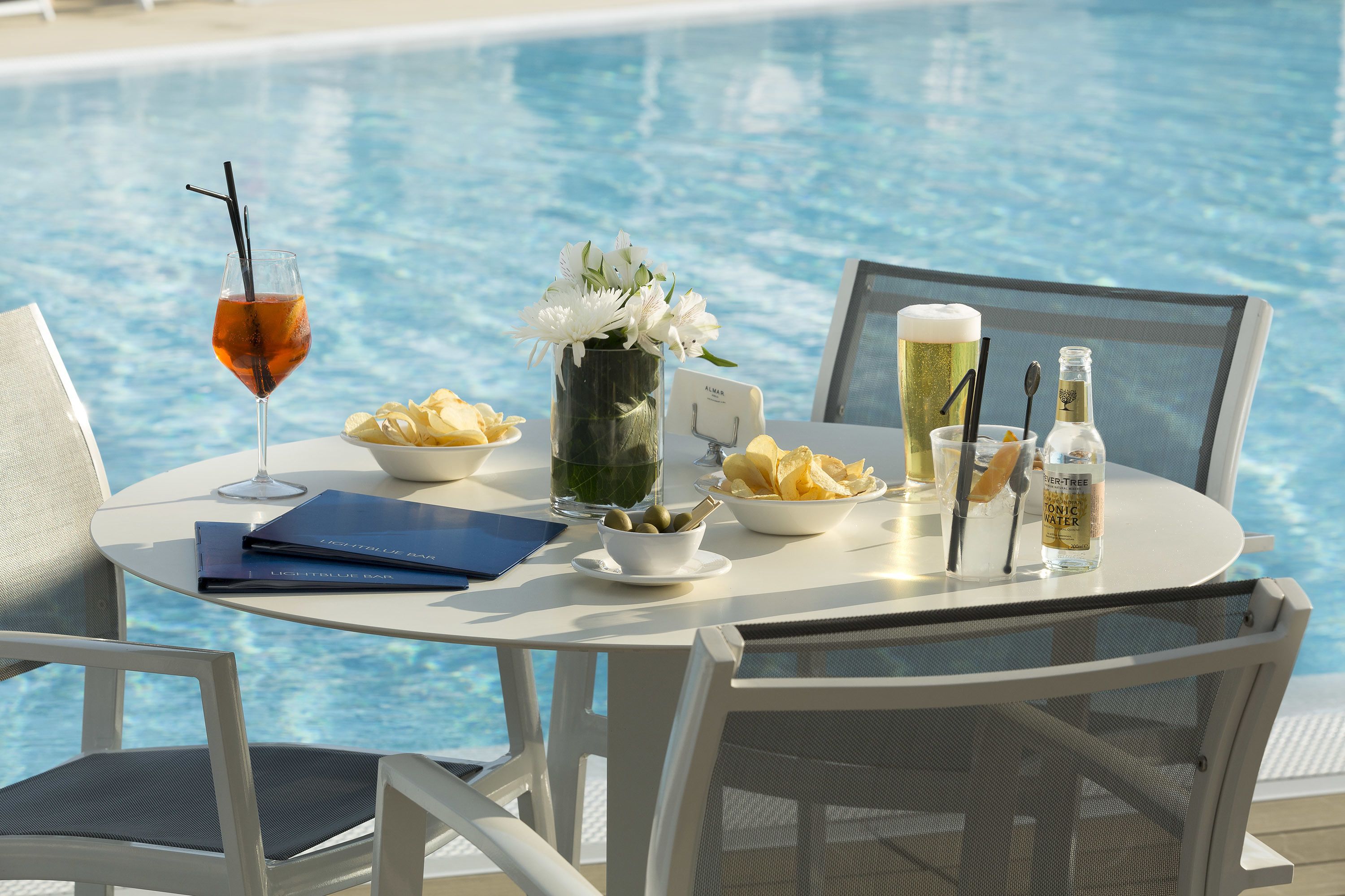 Spisebord ved en pool med is te, en skål chips, en vase med blomster, en menu og en vandflaske.