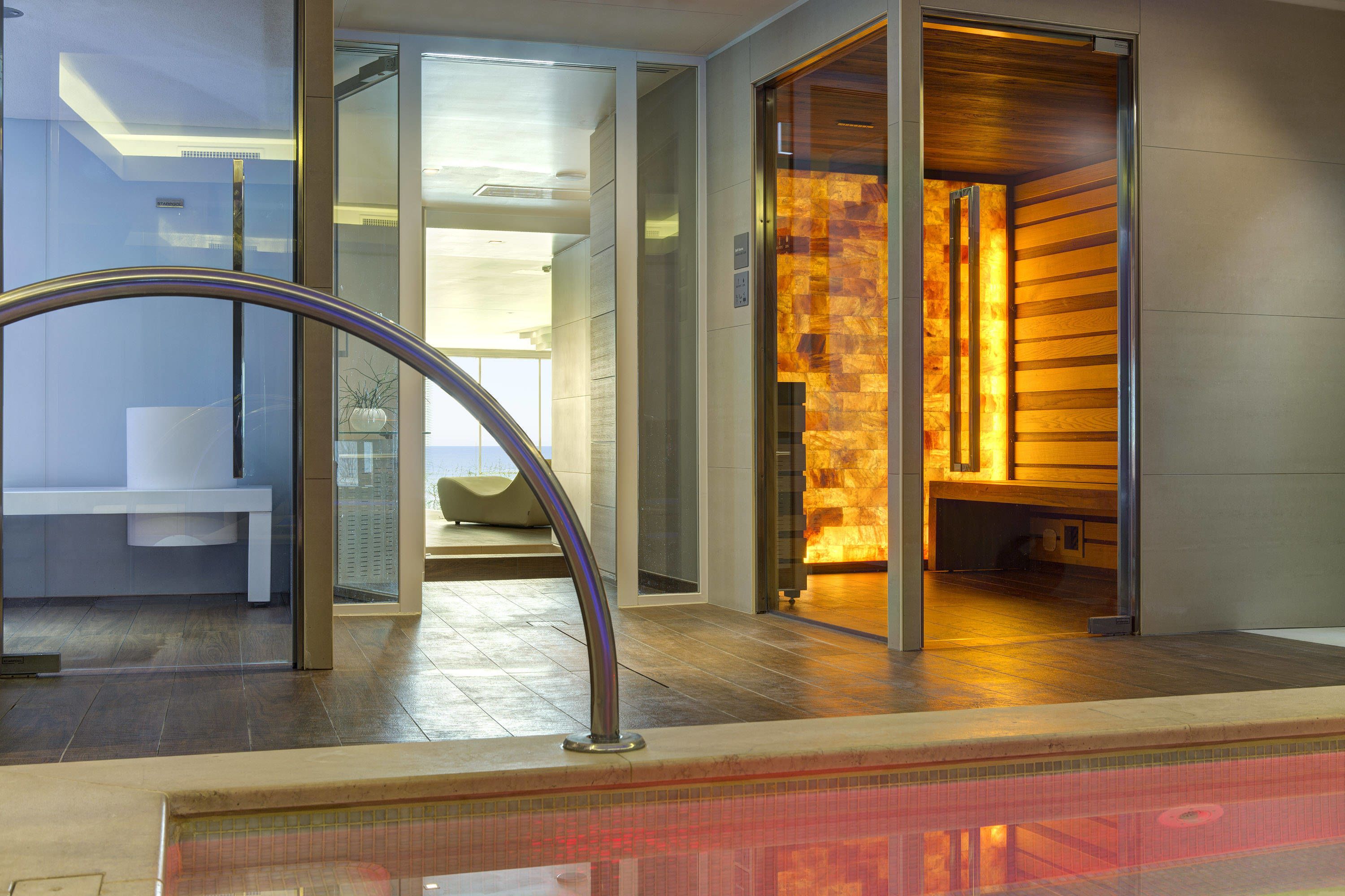 Un hall d’hôtel moderne avec une cloison en verre, un comptoir d’accueil et un éclairage intérieur chaleureux.