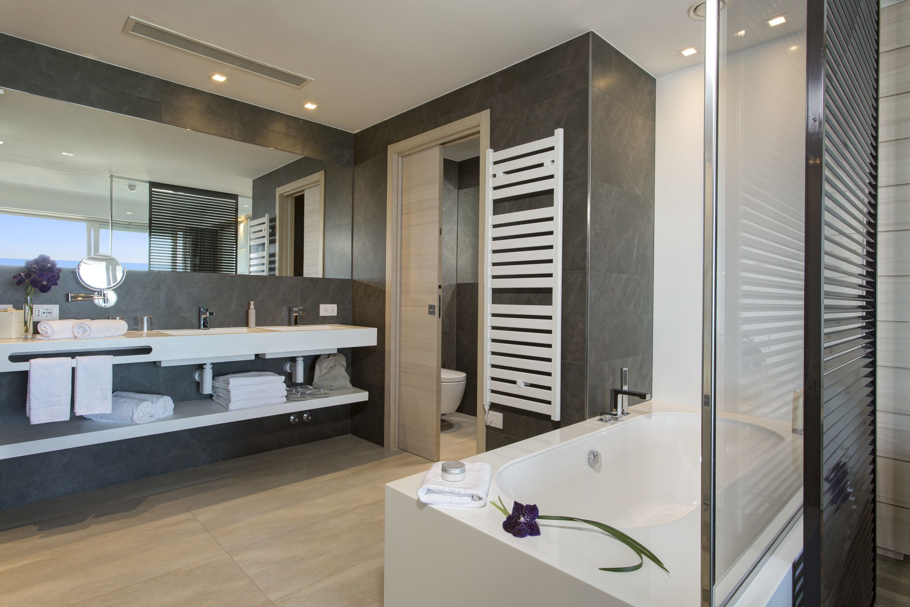 A modern bathroom with a large mirror, two sinks, a bathtub, and a glass shower enclosure.