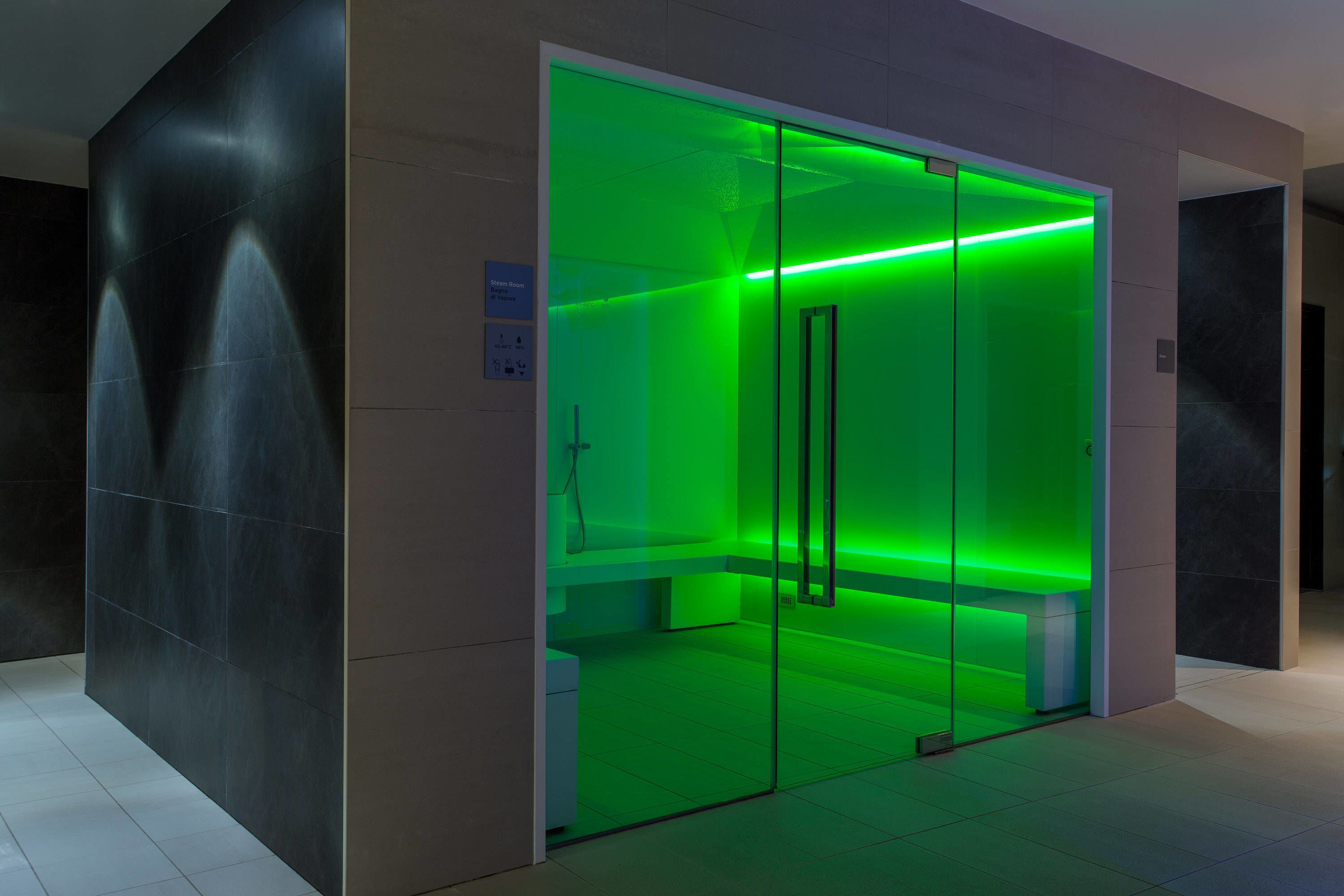 A modern elevator with green lighting, a glass door, and a bench inside.