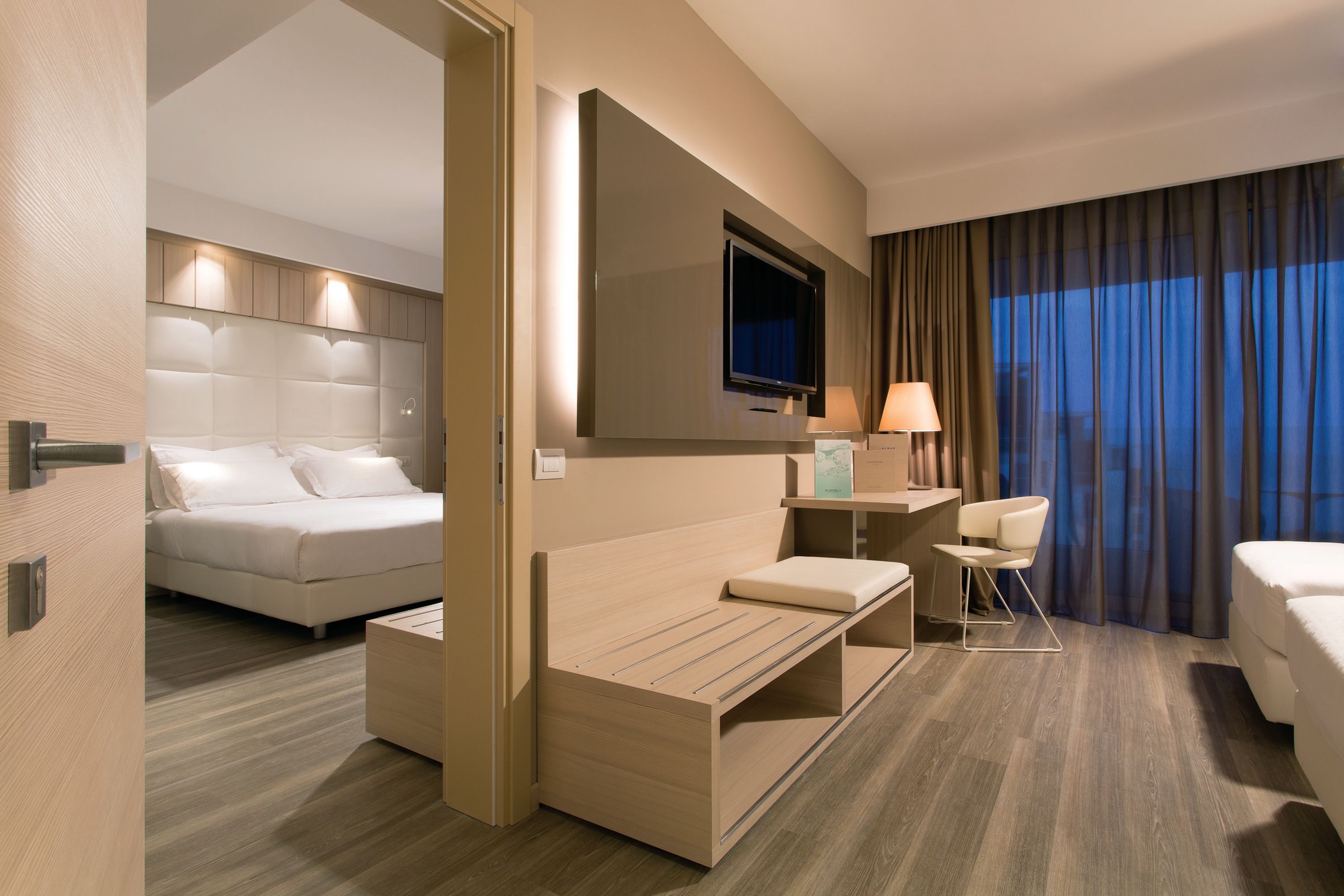 Quarto de hotel moderno com uma cama, um sofá, uma escrivaninha e uma televisão.