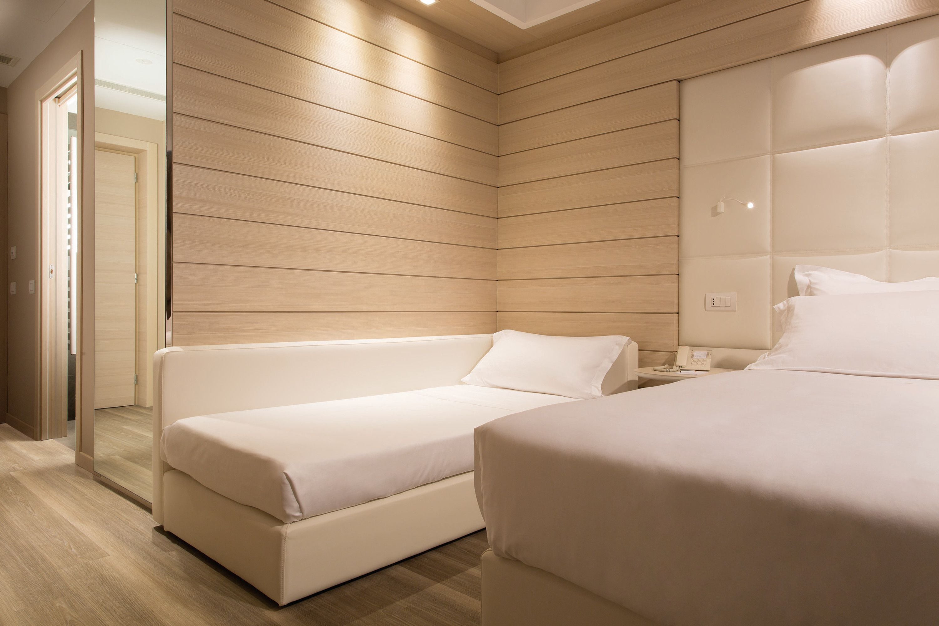 Une chambre d’hôtel moderne avec un mur lambrissé en bois, un canapé, un lit et une table de chevet.