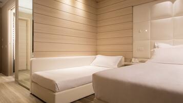 A modern hotel room with a wooden panel wall, a sofa, a bed, and a nightstand.