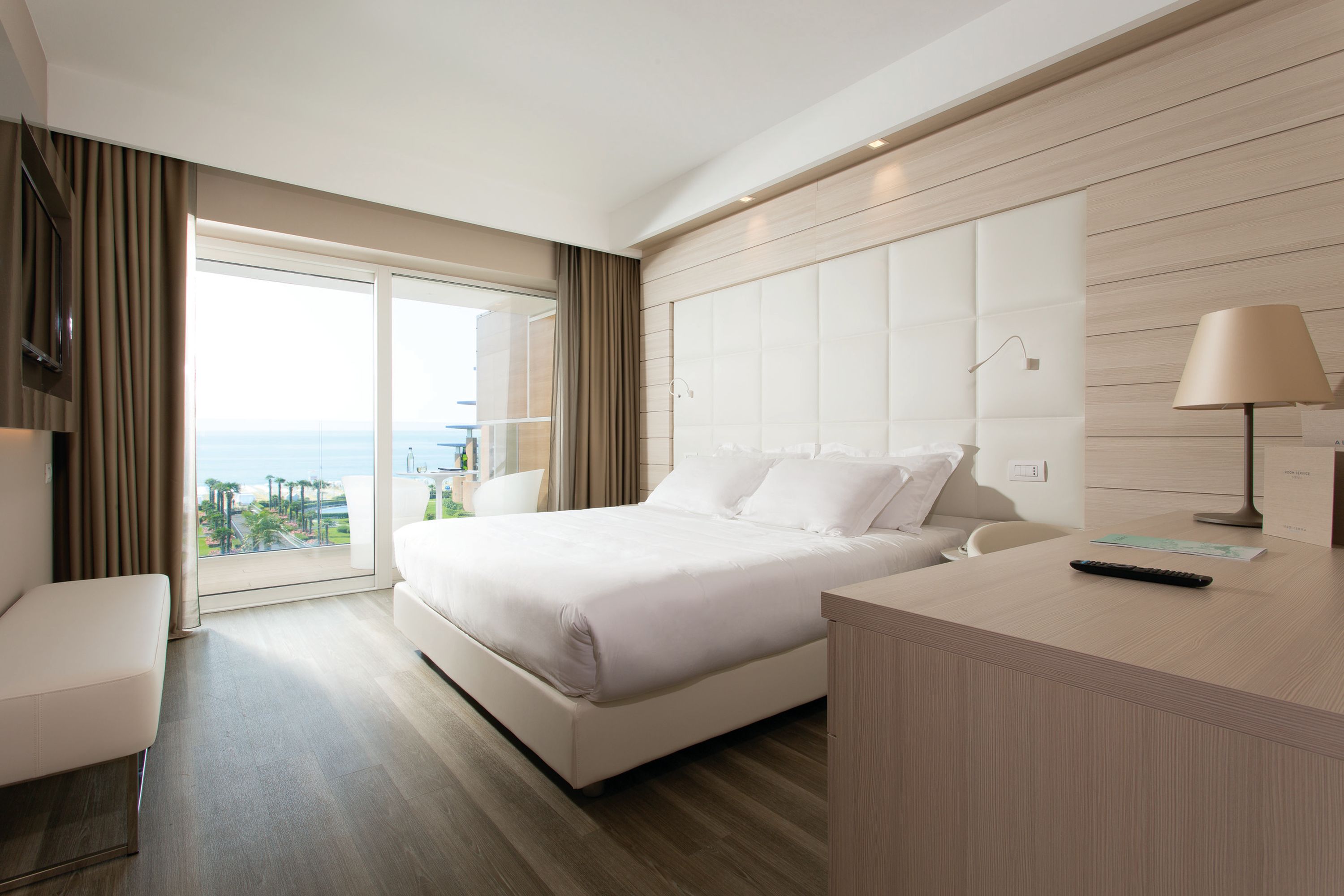 A modern hotel room with a large bed, a desk, and a view of the city.