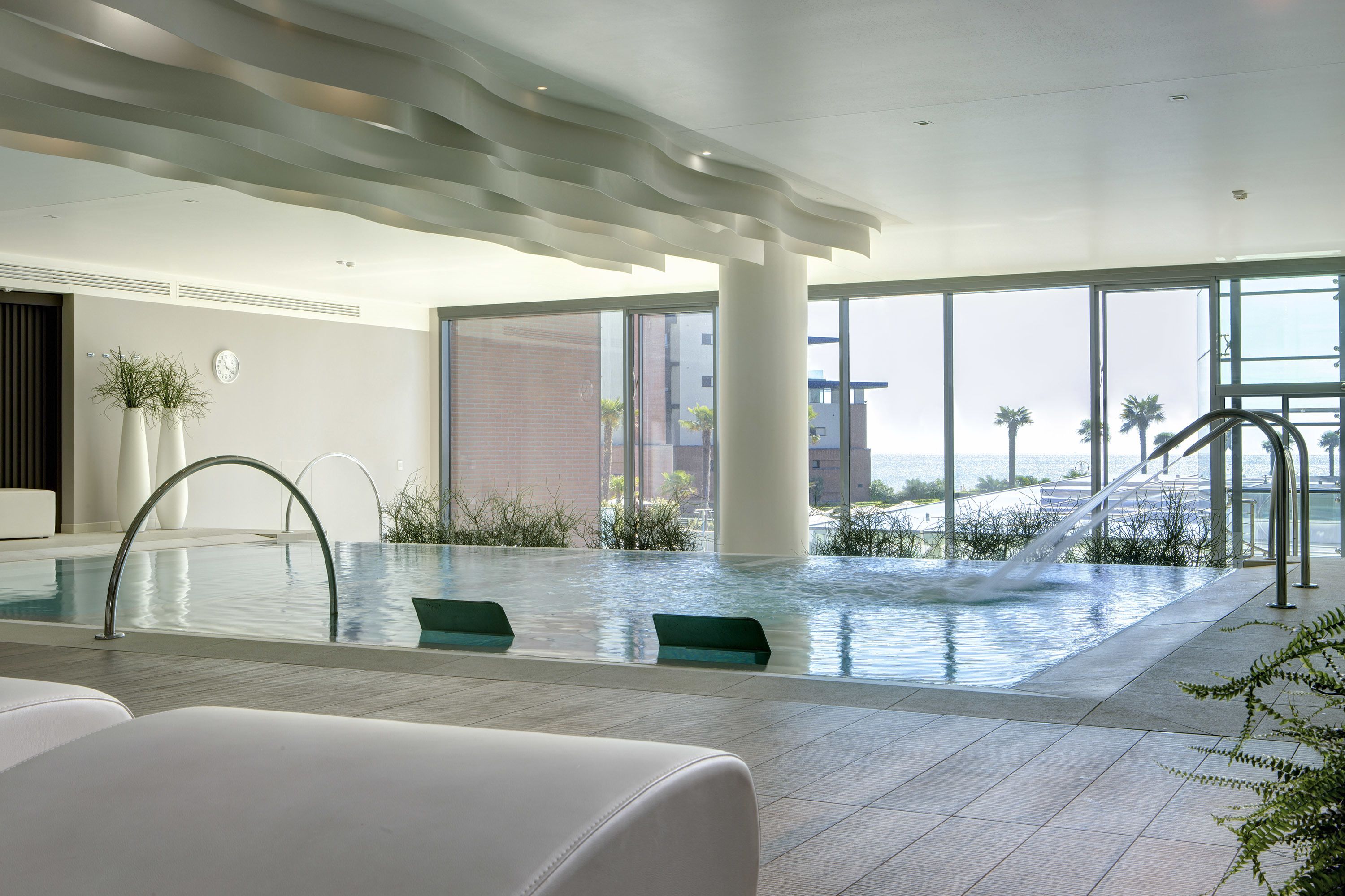 Uma piscina interior moderna com vista clara para o oceano, grandes janelas e um design minimalista.
