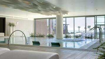 Uma piscina interior moderna com vista clara para o oceano, grandes janelas e um design minimalista.