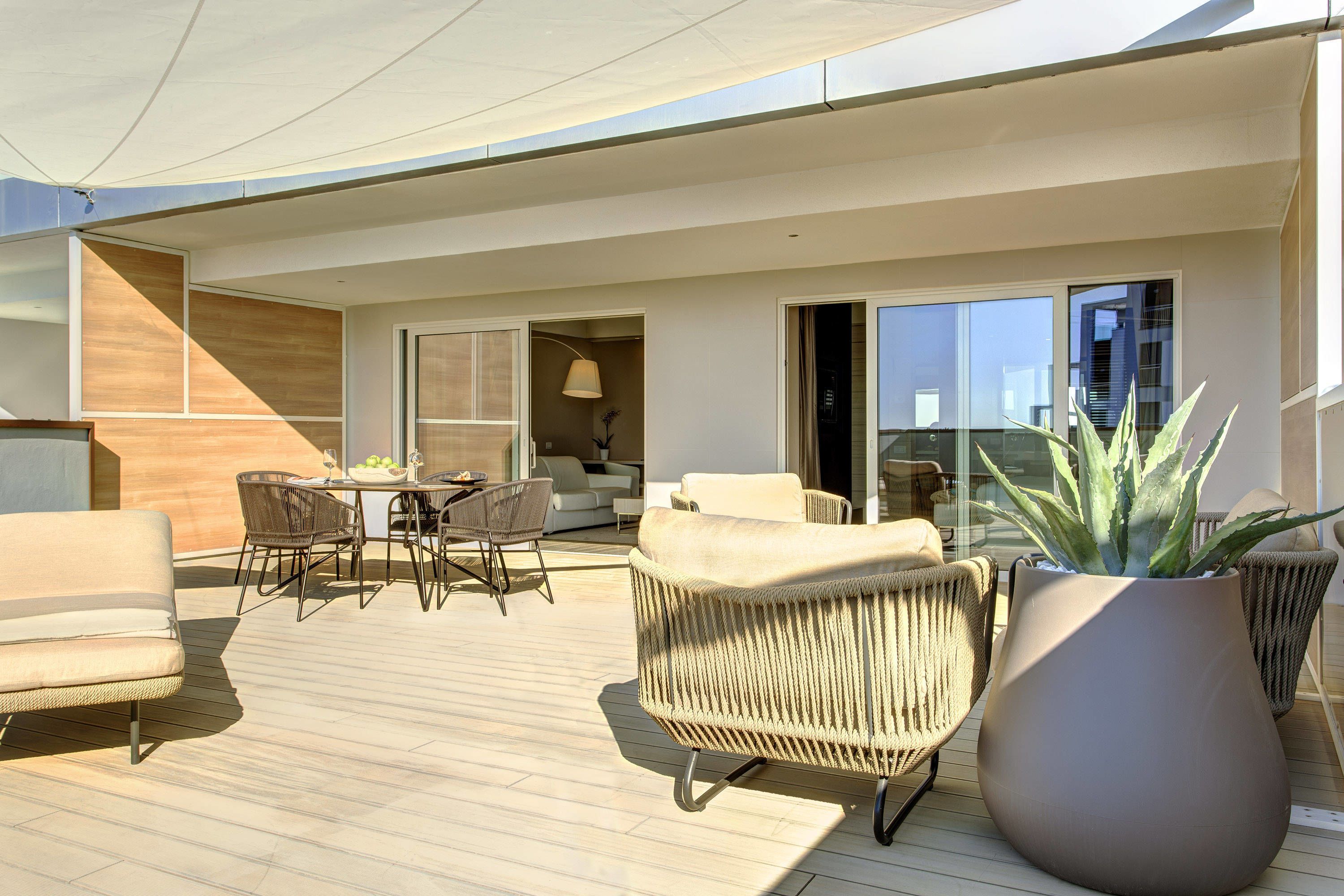 Un espace de vie extérieur moderne comprenant un ensemble de mobilier de salle à manger, des canapés et une grande plante en pot.