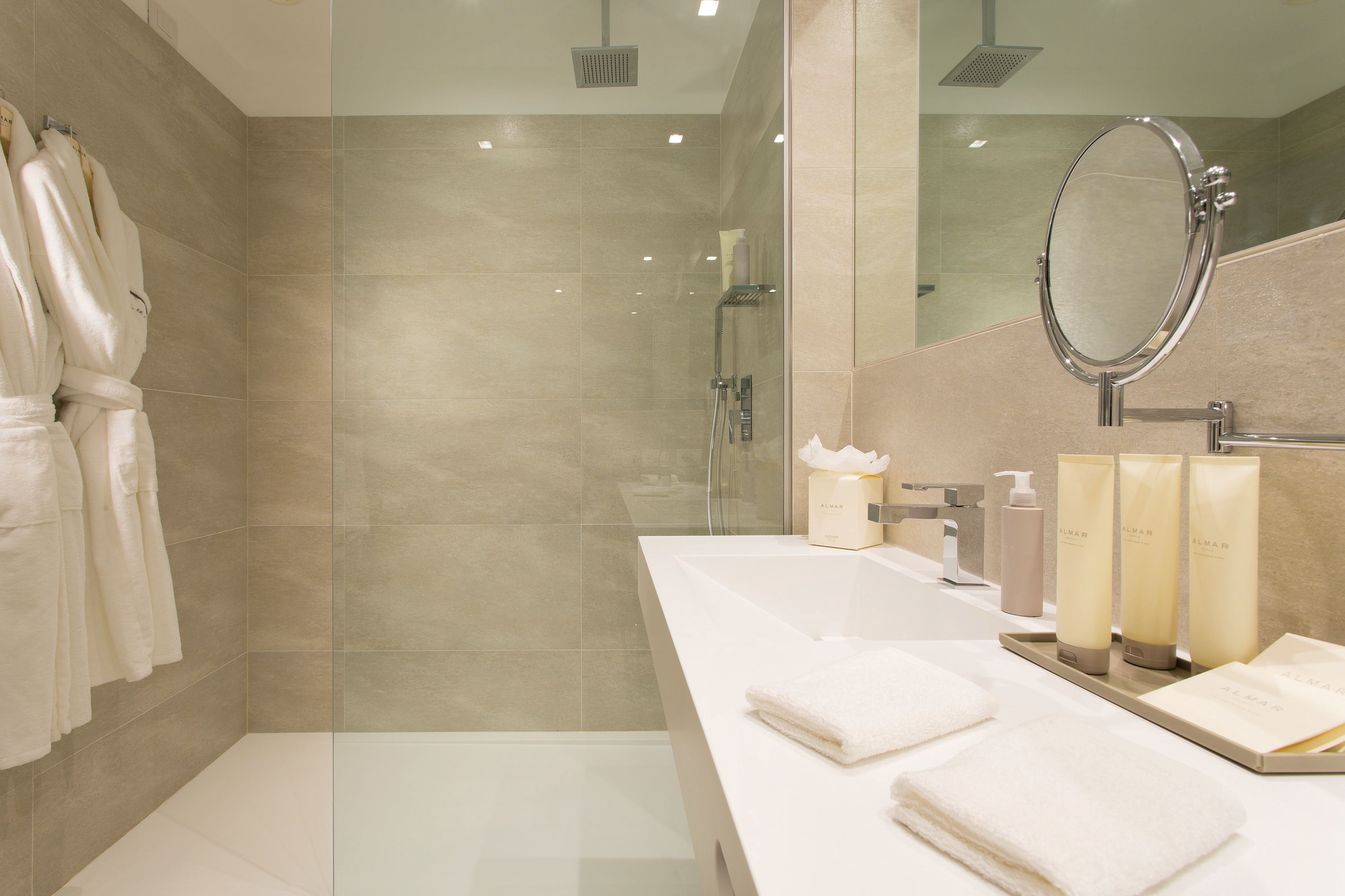 A modern bathroom with a glass shower enclosure, a large mirror, and a vanity with toiletries.