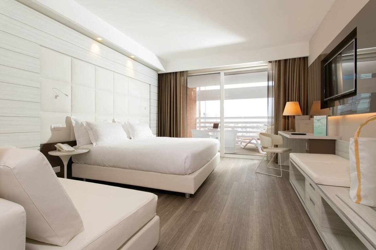 A modern hotel room with a large bed, a sofa, a desk, and a TV.