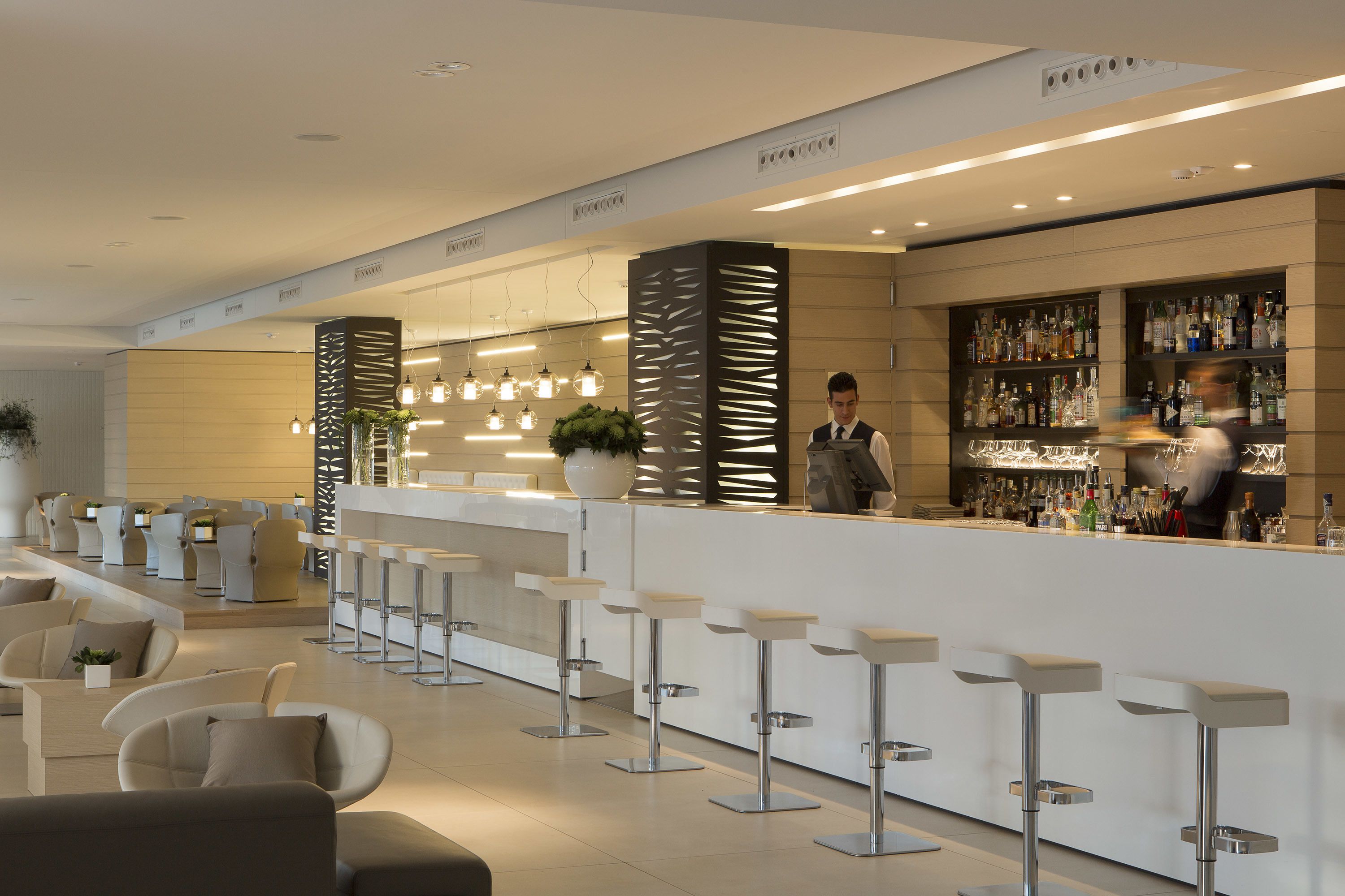 A modern bar area with a long counter, bar stools, and a bartender.