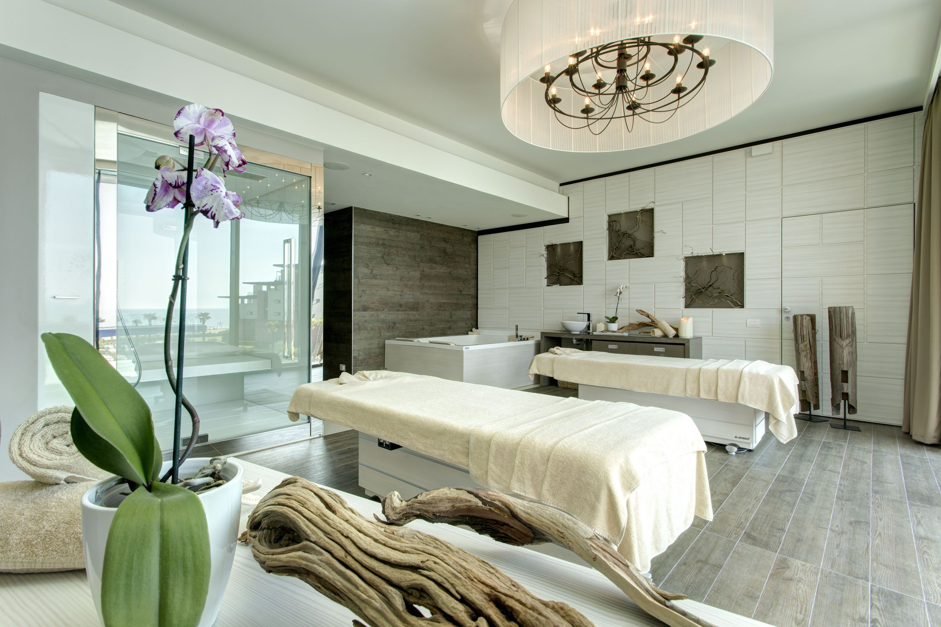 A modern spa room with a massage table, a large potted orchid, and a wooden sculpture.