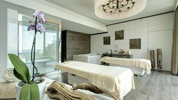 A modern spa room with a massage table, a large potted orchid, and a wooden sculpture.