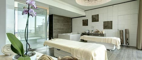 Un spa moderno con una camilla de masaje, una orquídea grande en maceta y una escultura de madera.