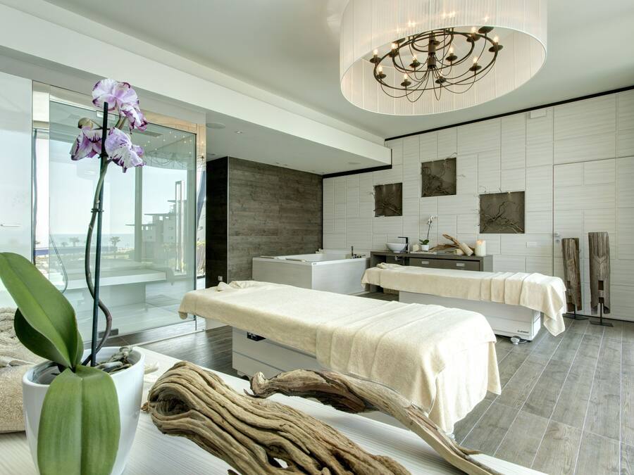 A modern spa room with a massage table, a large potted orchid, and a wooden sculpture.