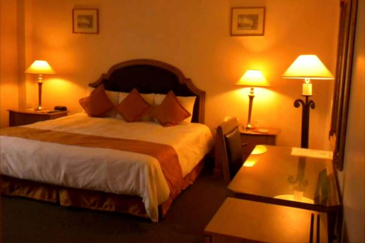 Una habitación de hotel con una cama, dos mesitas de noche con lámparas, una silla y un escritorio con lámpara.