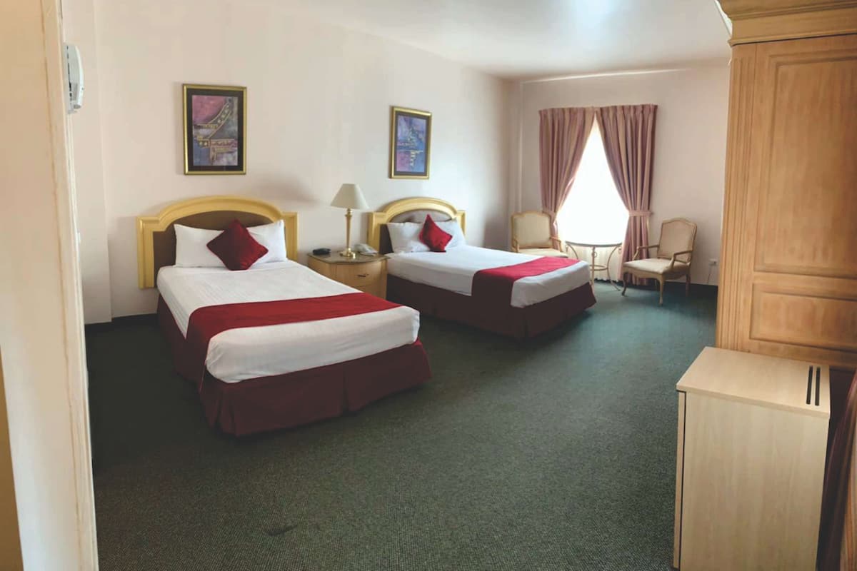 Habitación de hotel con dos camas, un escritorio, una silla y un armario.