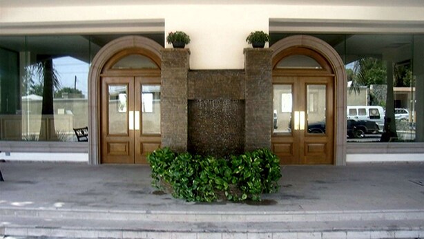 A building entrance with two arched doors, a stone wall, and a small garden area. - Best Western Centro Cadereyta (Cadereyta Jimenez)