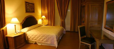 A hotel room with a bed, a desk, a chair, and a nightstand with lamps.
