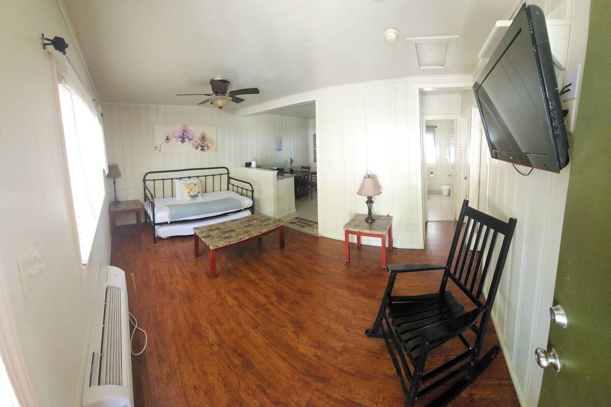 A room with a bed, a rocking chair, a television, and a small table with a lamp.