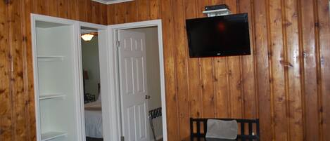 A room with wooden panel walls, a flat-screen TV mounted above a bench, and a door leading to another room.