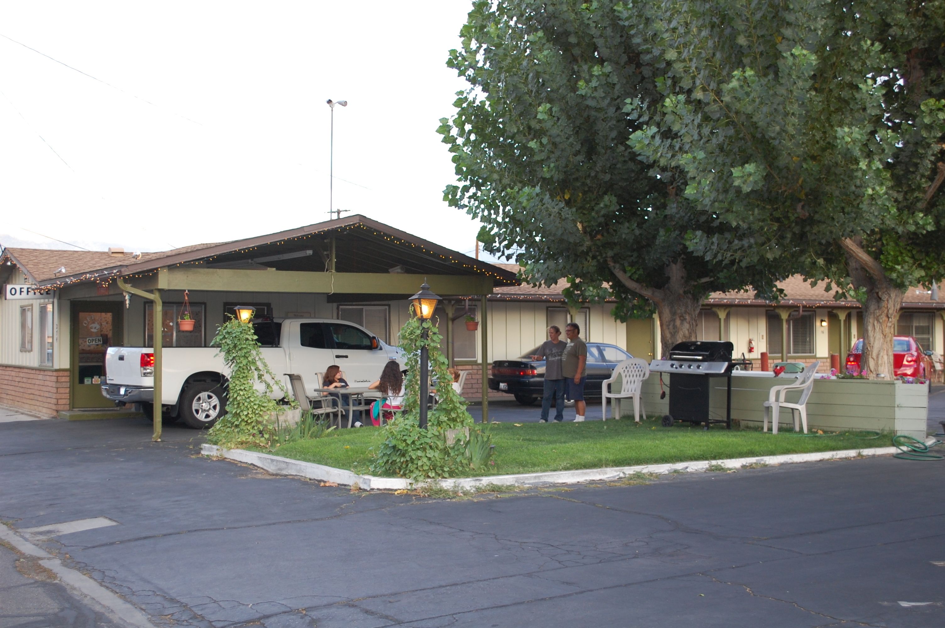 Un motel con una zona de estar al aire libre cubierta, una parrilla y una camioneta pickup blanca estacionada afuera.