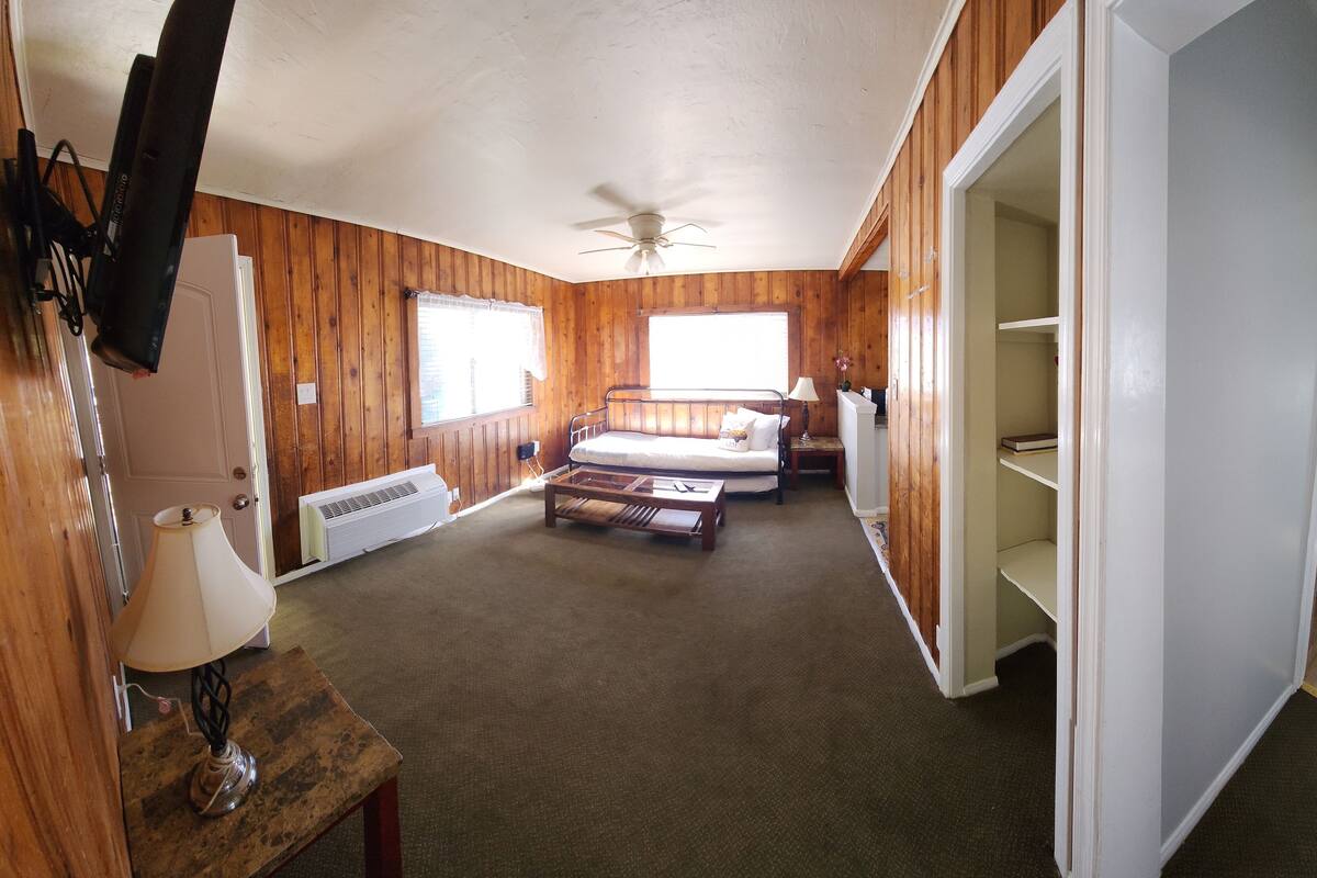 A room with a bed, a desk, a chair, a ceiling fan, and a bathroom visible through an open door.