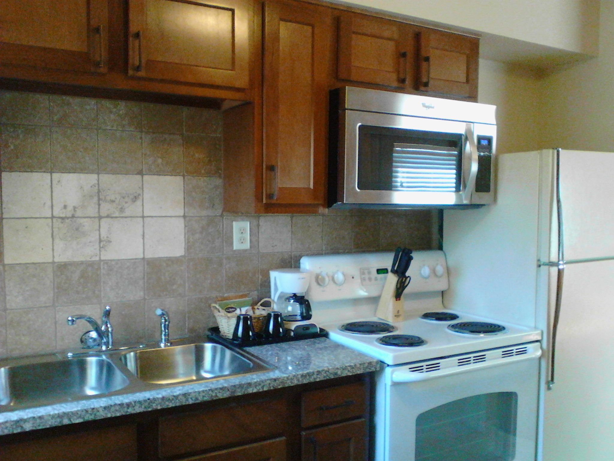 A kitchen with wooden cabinets, a stainless steel microwave, a white stove, and a sink.