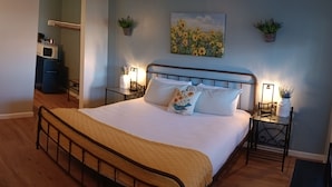 A bedroom with a bed, bedside tables, a nightstand, a wooden bench, a small table with a jar, and a wall-mounted plant.