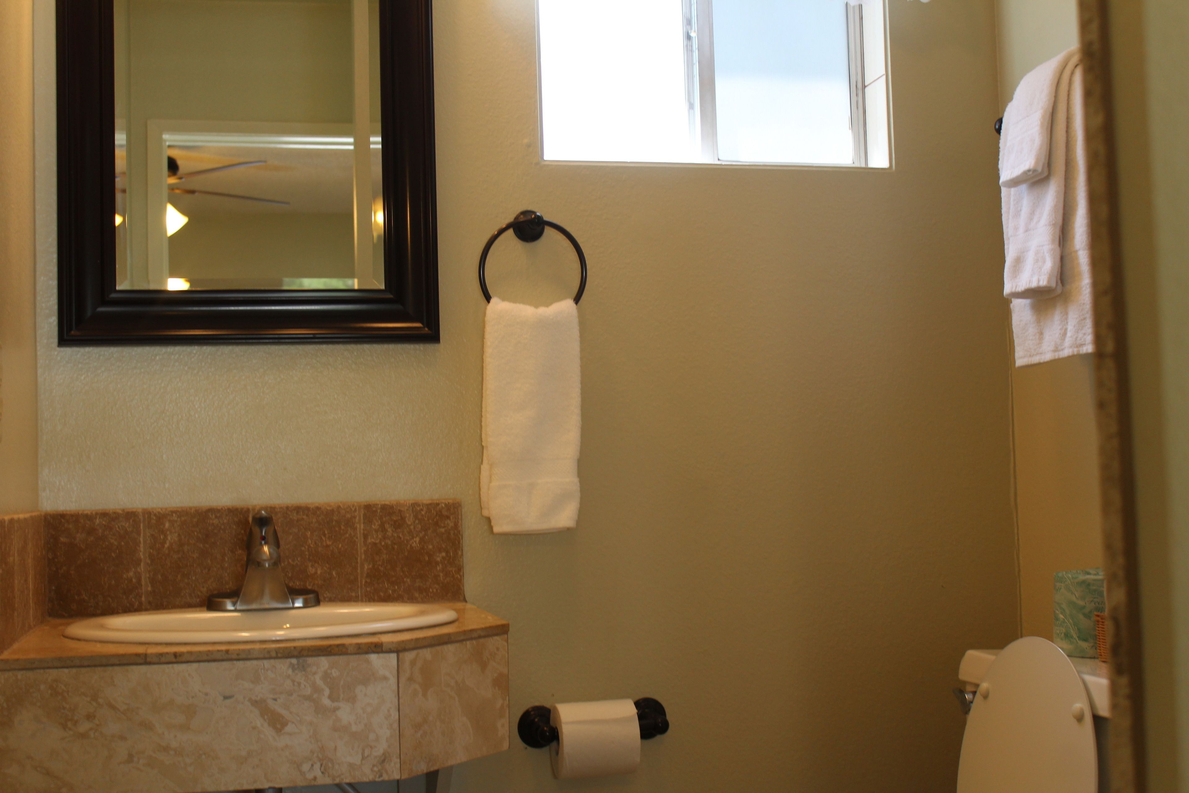 A bathroom with a sink, mirror, towel rack, toilet, and a window.