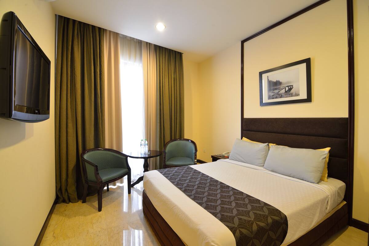 A hotel room with a bed, two chairs, a small table, a TV, and a framed picture on the wall.