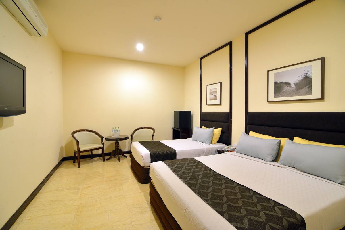A hotel room with two beds, a desk, chairs, a flat-screen TV, and framed pictures on the walls.