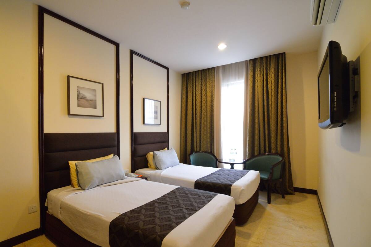 A hotel room with two beds, a desk, a chair, a TV, and a window with curtains.