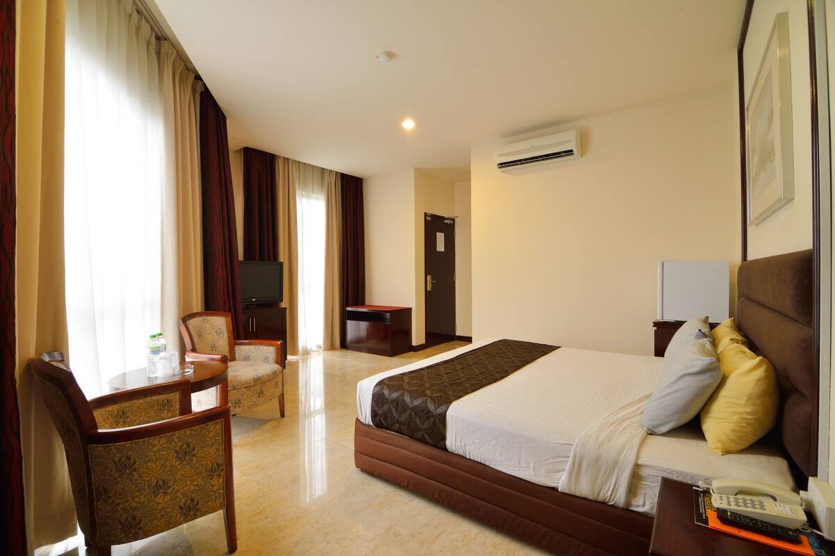 A hotel room with a bed, a desk with a chair, a television, and an air conditioning unit.