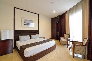 A hotel room with a large bed, a desk, two chairs, a small table, a refrigerator, and a framed picture on the wall. - Media Hotel (Petaling Jaya)
