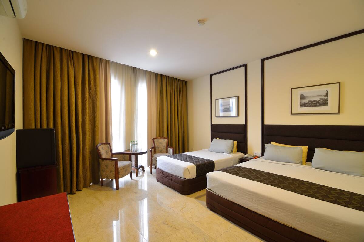 A hotel room with two beds, a desk with a chair, a TV, and a window with curtains.