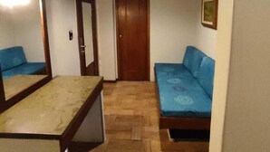 Ein kleiner, gemütlicher Raum mit Holzbalkendecke, einem Bett mit blauer Bettwäsche, einem kleinen Tisch und einem Spiegel an der Wand.
