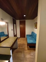 Una habitación pequeña y acogedora con techo de madera, una cama con ropa de cama azul, una mesita y un espejo en la pared.