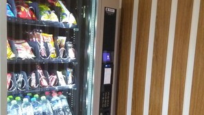 Ein Verkaufsautomat mit verschiedenen Snacks und Getränken, einem Bezahlsystem und einem Schild mit der Aufschrift 'RETIRE SEU PRODUTO'.