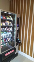 Una máquina expendedora con diferentes snacks y bebidas, un terminal de pago y un letrero que dice "RETIRE SEU PRODUTO".