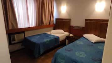 A hotel room with two single beds, a window with curtains, a wall-mounted heater, and a nightstand with a phone.