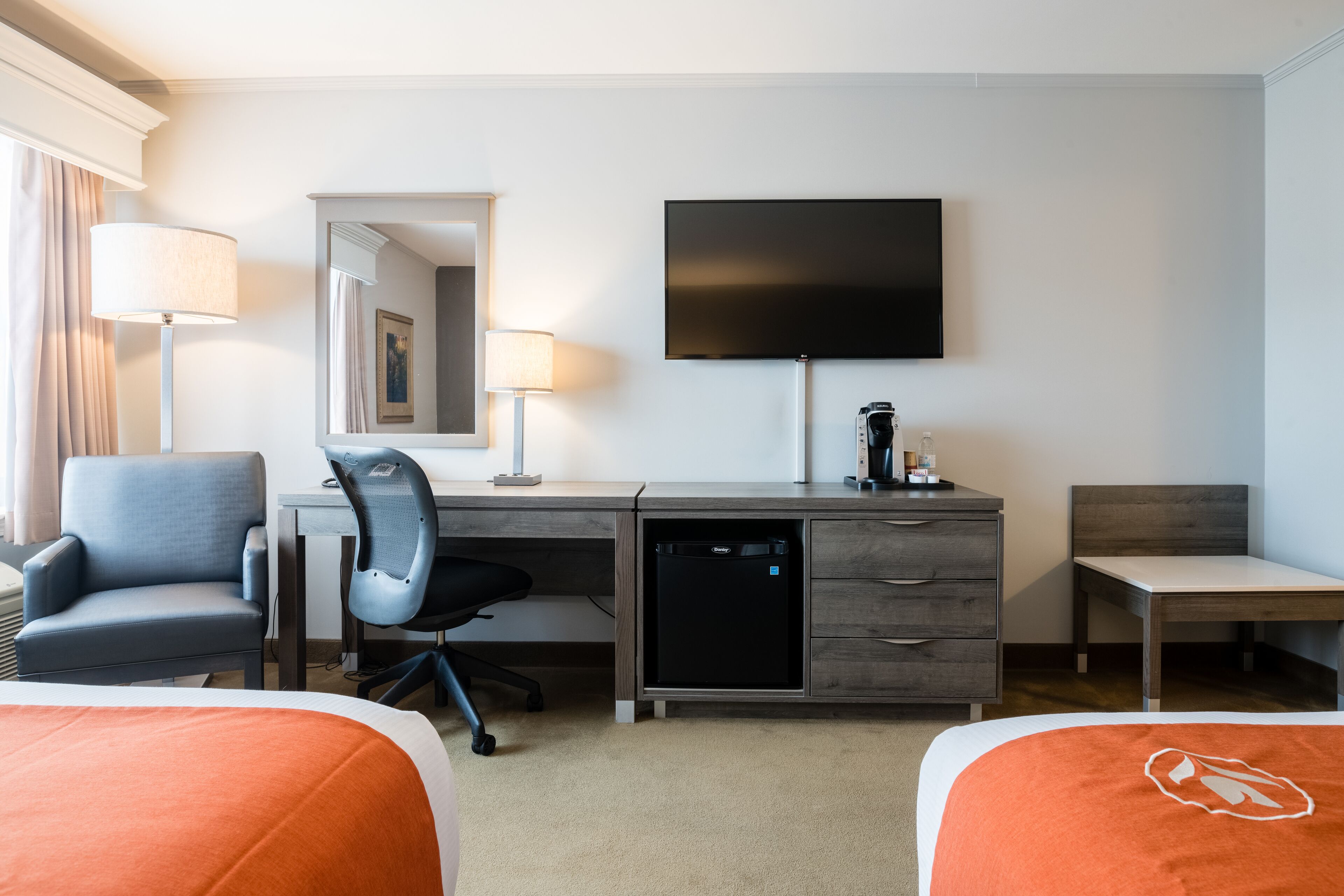 A hotel room with a bed, a desk with a chair, a television, a coffee maker, and a small refrigerator.