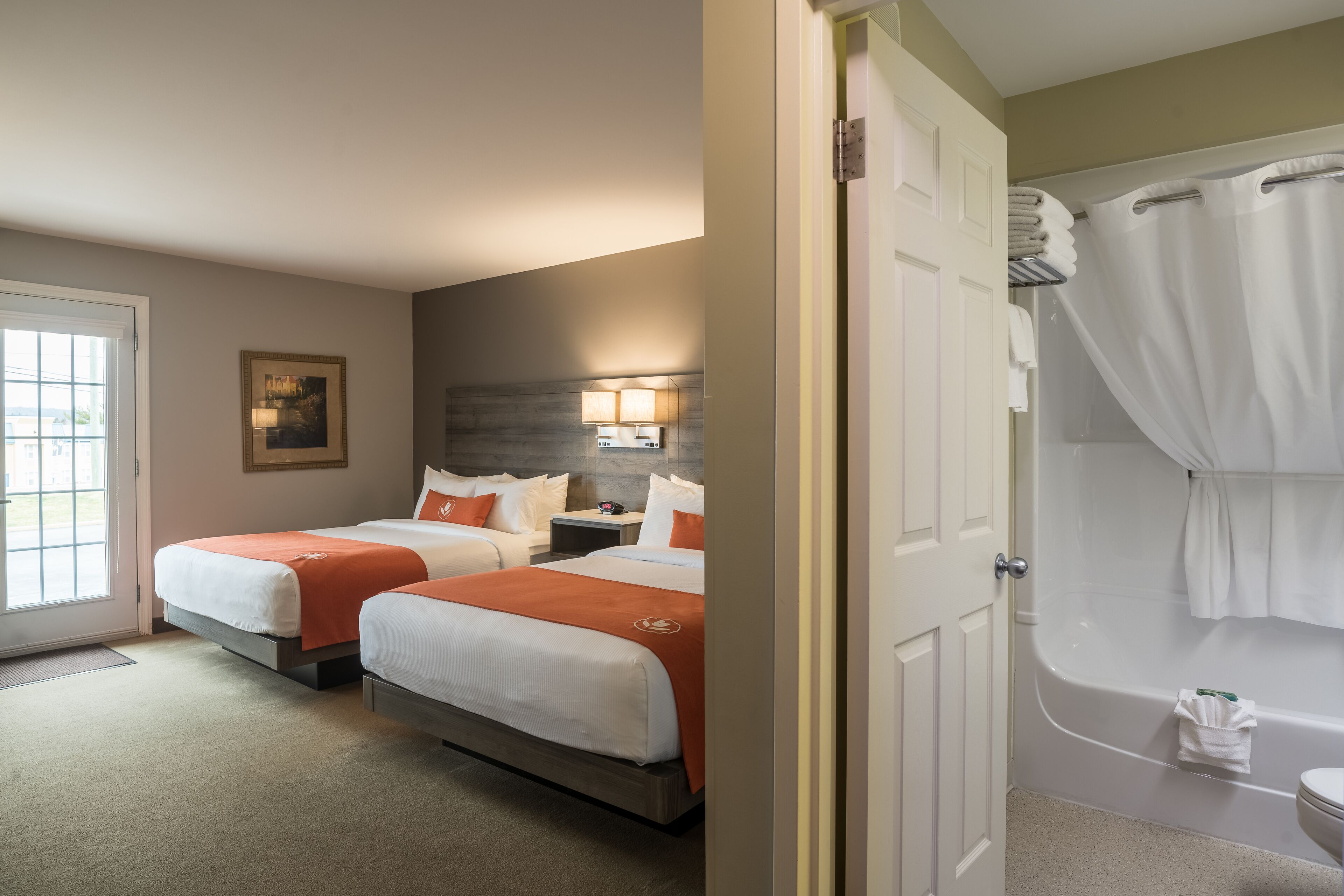 A hotel room with two beds, a bathroom with a bathtub, and a door leading to another room.