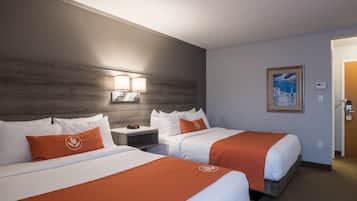 Habitación de hotel con dos camas, cada una con ropa blanca y detalles naranja, una mesita de noche con lámpara, un cuadro en la pared y una puerta a la derecha.