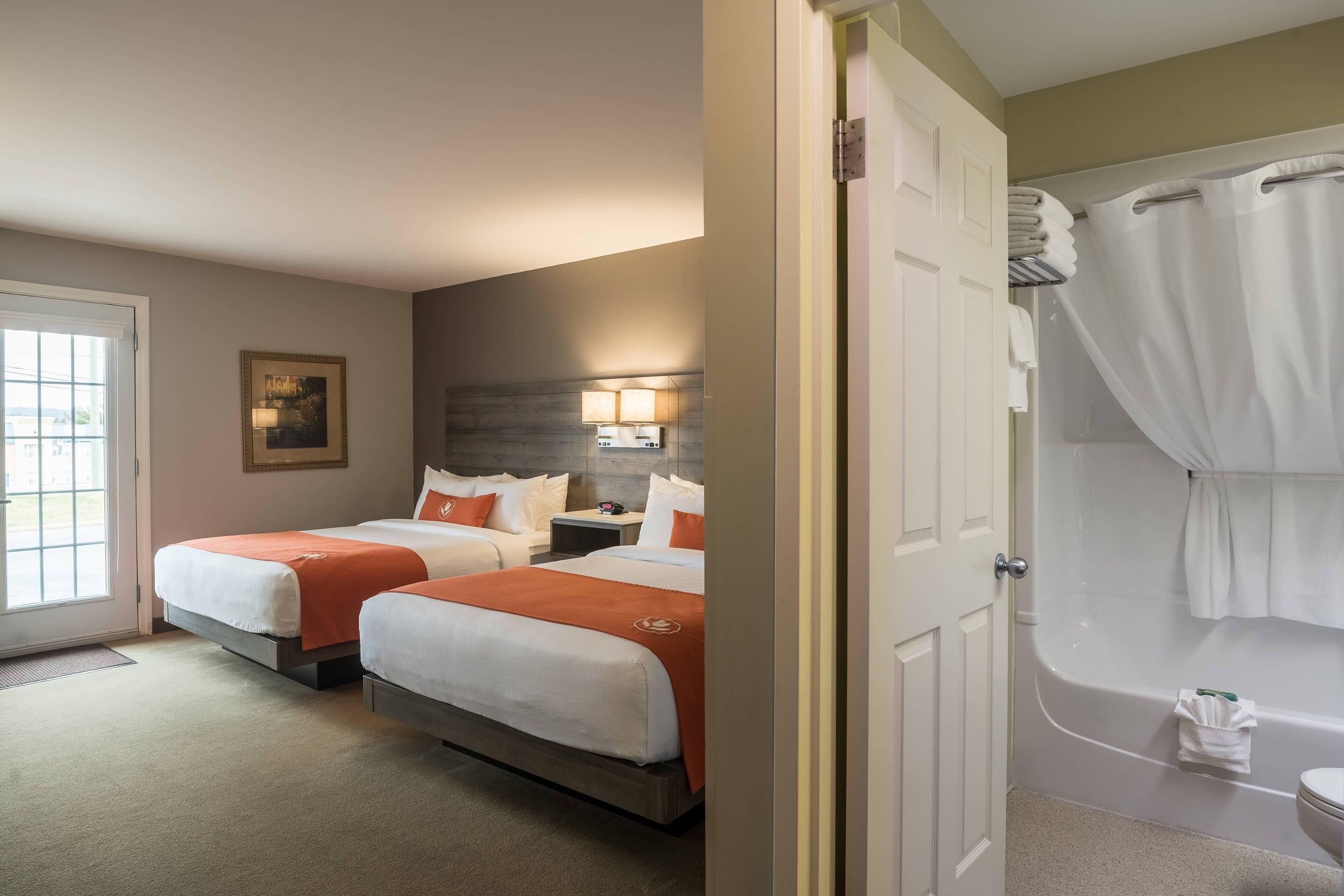 A hotel room with two beds, a bathroom with a bathtub, and a door leading to another room.