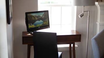 A computer desk with a monitor displaying a scenic landscape, a chair, and a floor lamp.