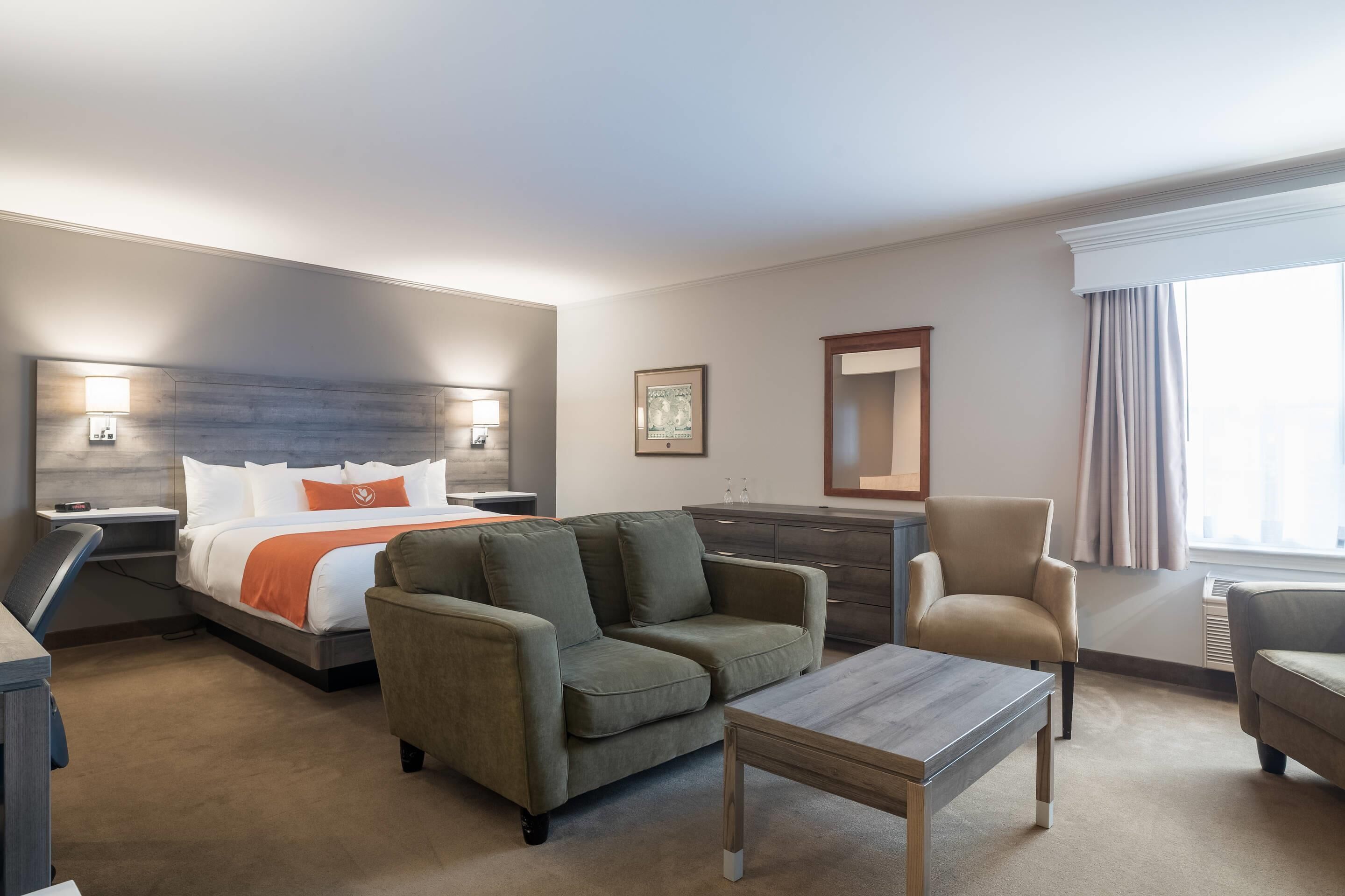 A hotel room with a bed, two sofas, a coffee table, a desk, and a dresser.